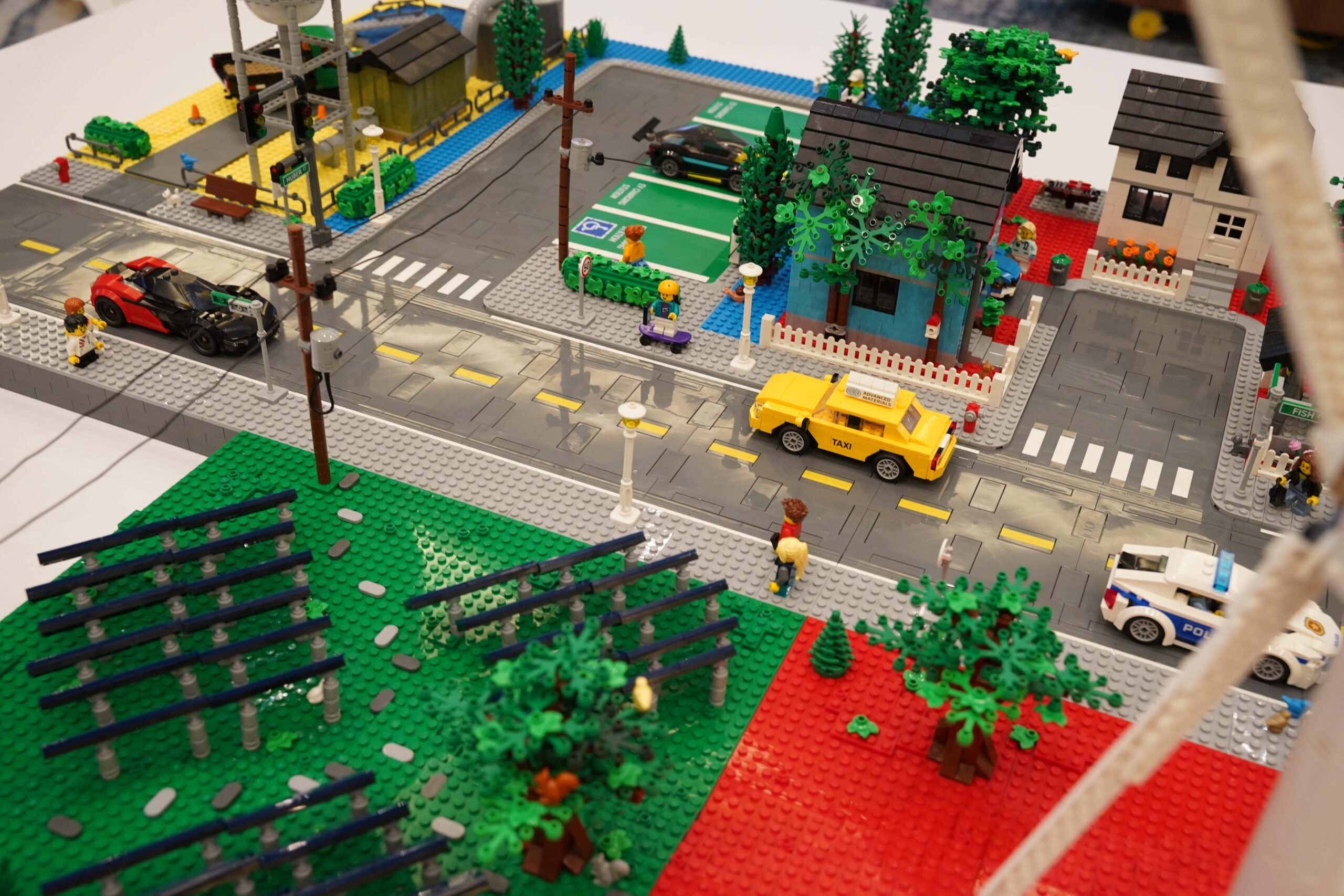 Overhead detail of the LEGO city roads, houses, solar arrays, EV charging, and Huber taxi