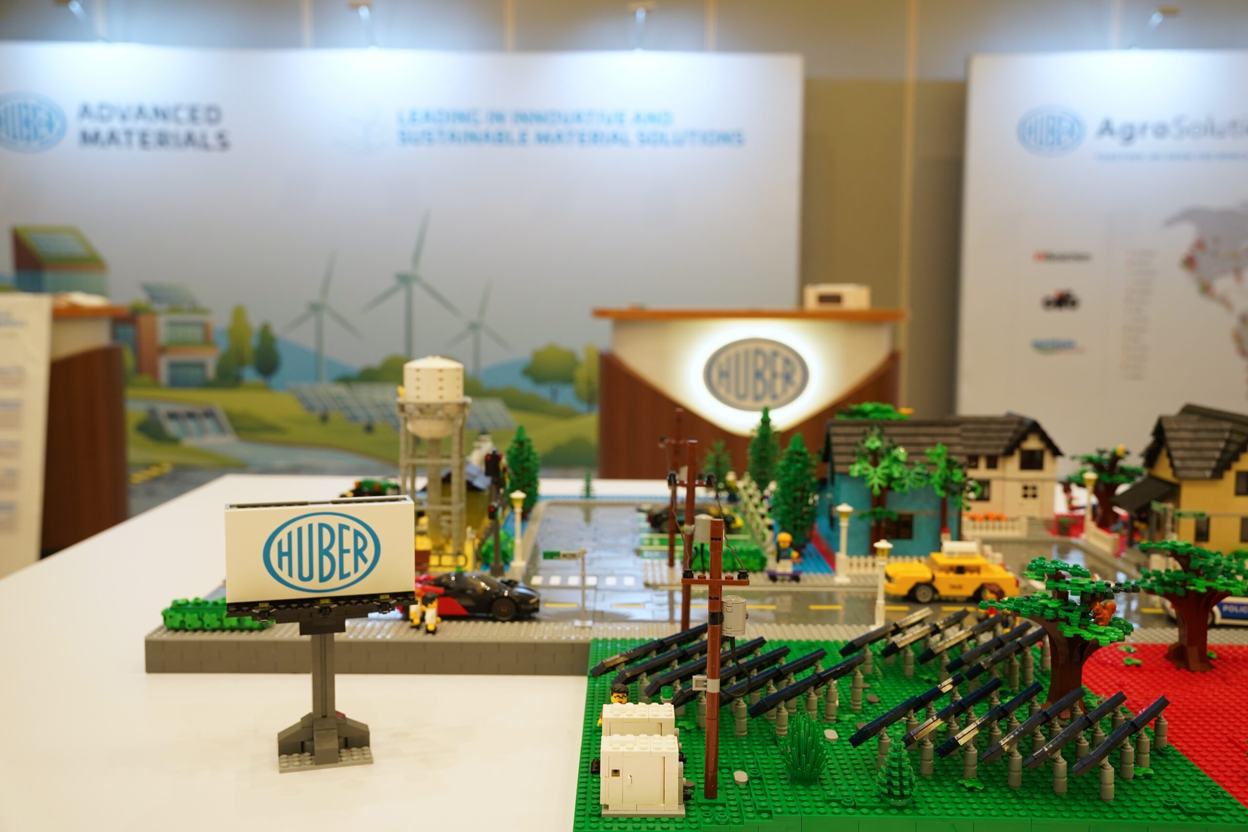 Custom Huber Advanced Materials LEGO city display shown at HUBERpalooza with Huber booth branding in the background